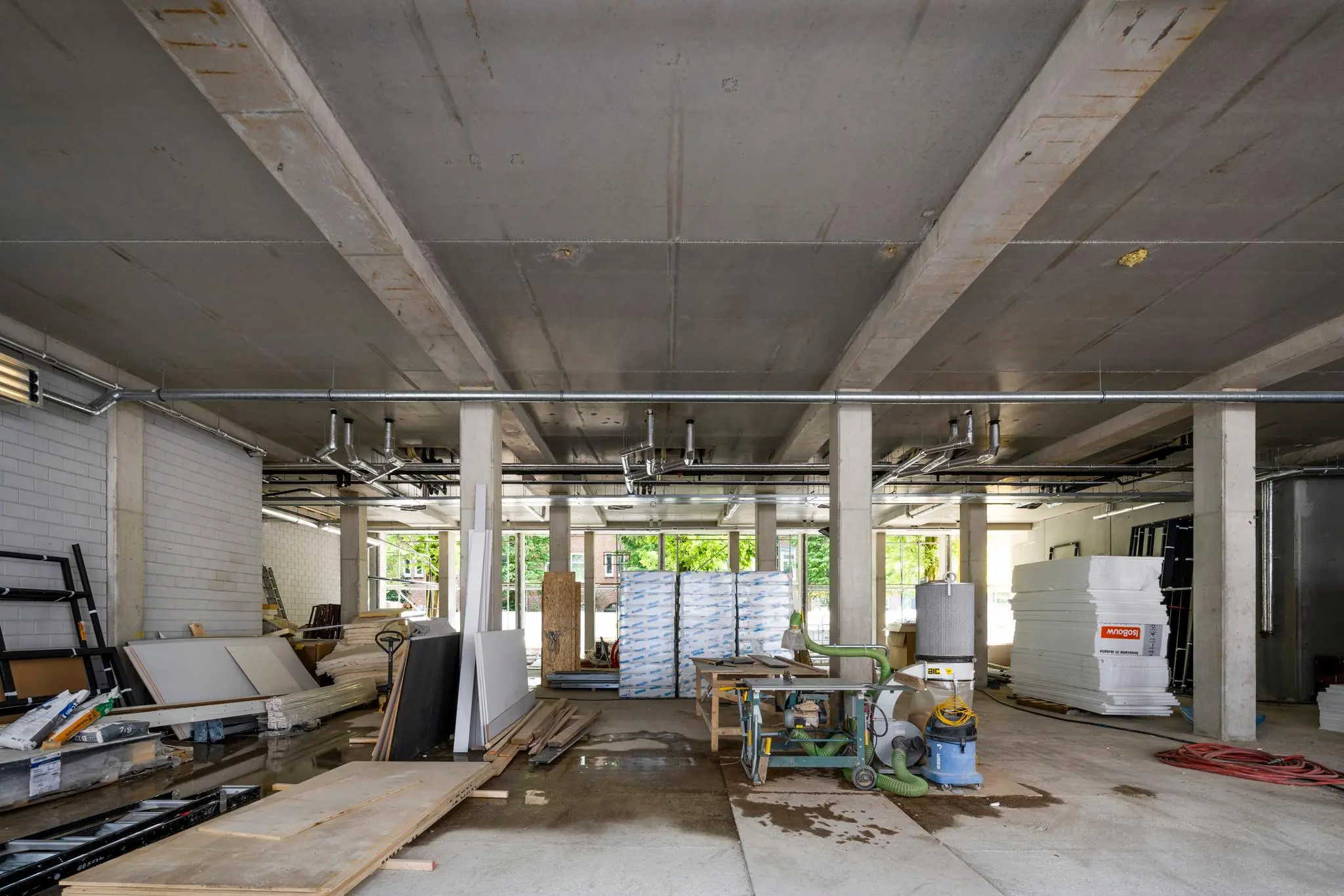 Ruimte in aanbouw aan de Karel du Jardinstraat met bouwmaterialen, machines en betonnen pilaren.